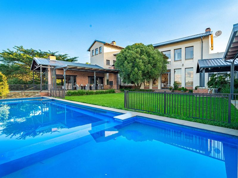 A spacious rear garden featuring a large swimming pool, a covered patio area, and a multi-story residence with expansive windows.
