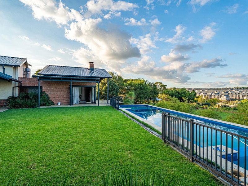 A well-maintained rear garden featuring a swimming pool with safety fencing, a covered patio area, and expansive views of the surrounding neighborhood.