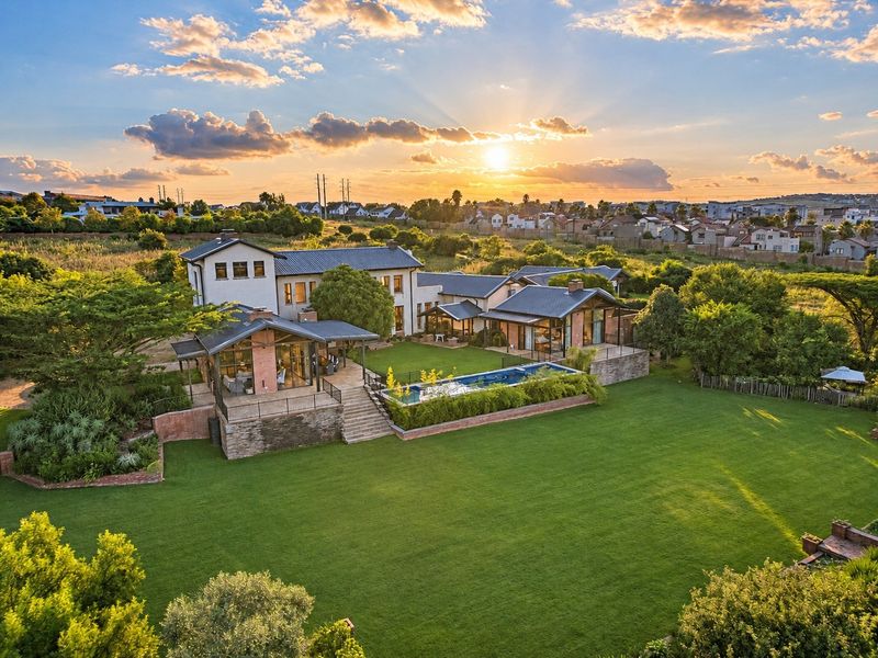 Stunning aerial view of a luxury residence featuring a large landscaped garden, swimming pool, and expansive covered patio areas at sunset.