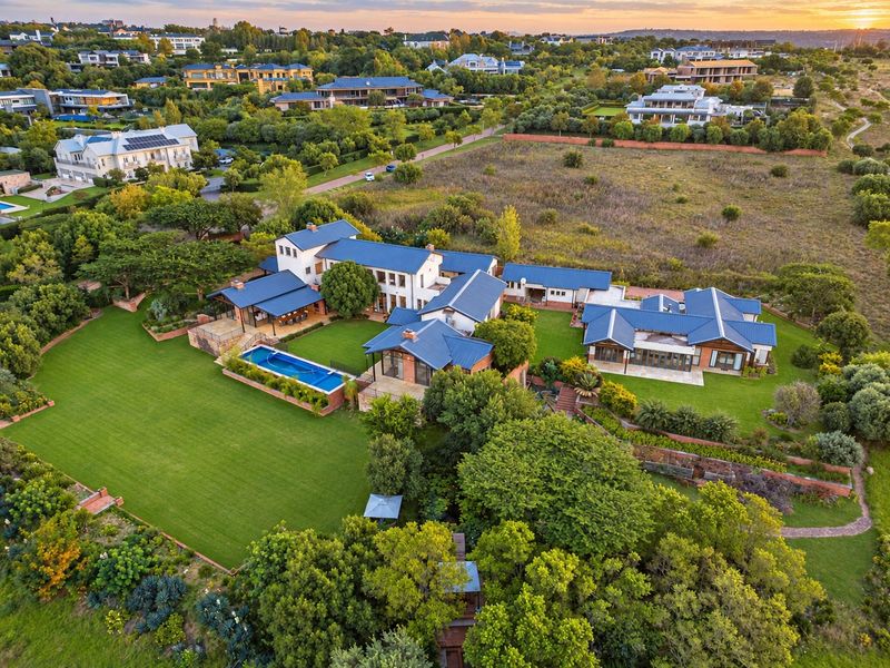 Aerial view of a large residential estate featuring multiple interconnected buildings, a swimming pool, expansive lawns, and mature landscaping in a scenic setting.