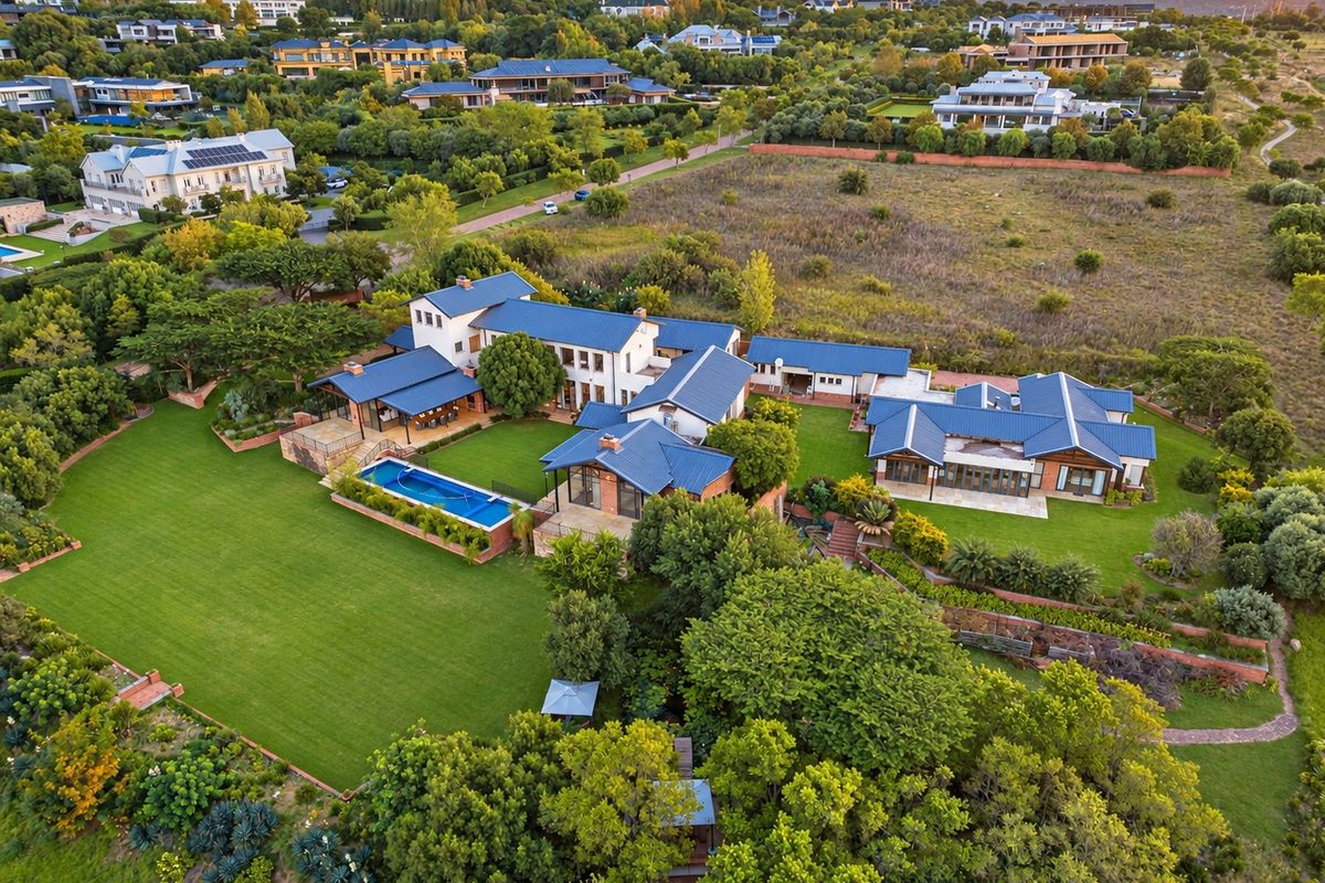 Aerial view of a large residential estate featuring multiple interconnected buildings, a swimming pool, expansive lawns, and mature landscaping in a scenic setting.