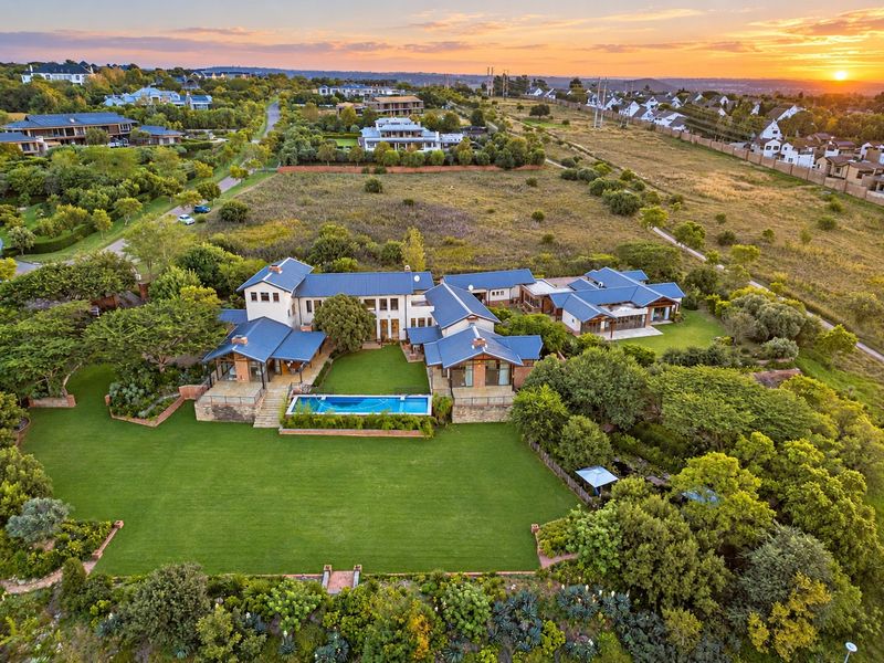 Aerial view of a large residential estate featuring a sprawling landscaped garden, swimming pool, and multiple interconnected building wings with metal roofing.