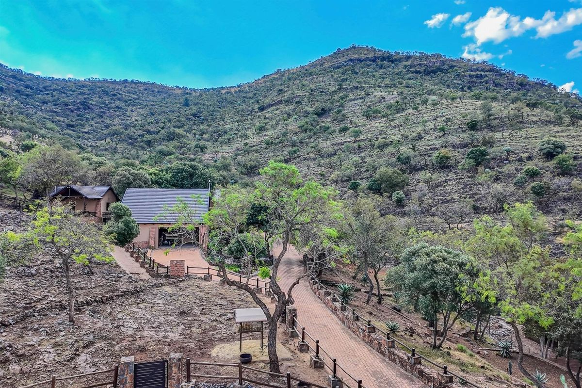 An elevated view of a small holding property featuring a paved driveway, stone-accented structures, and established trees set against a scenic mountain backdrop.