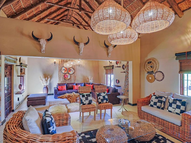 Spacious open-plan living area featuring a high vaulted thatched roof with exposed timber rafters, stone accents, and tiled flooring.