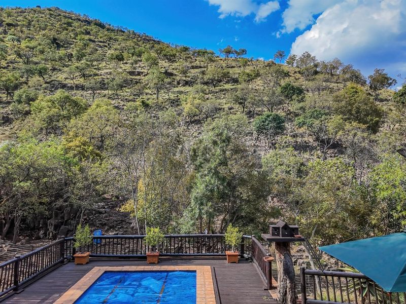 An elevated timber deck featuring a swimming pool, overlooking a lush, natural hillside landscape.