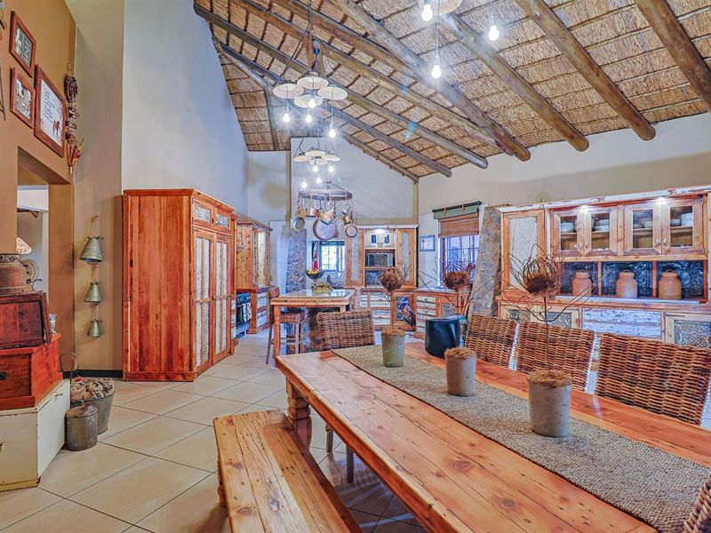 Spacious open-plan living and kitchen area featuring a high exposed thatch ceiling with timber trusses, custom wooden cabinetry, and tiled flooring throughout.