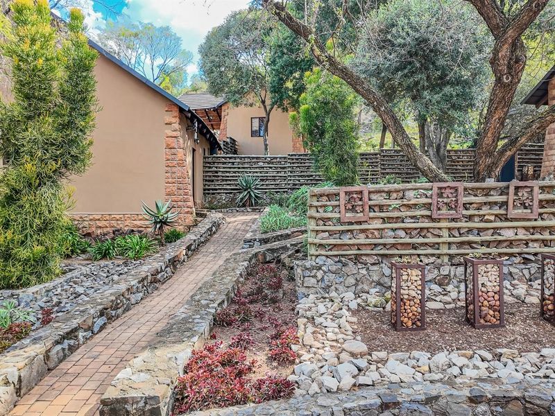 A well-maintained garden area featuring stone masonry, brick pathways, and decorative timber and gabion fencing elements within a small holding property.