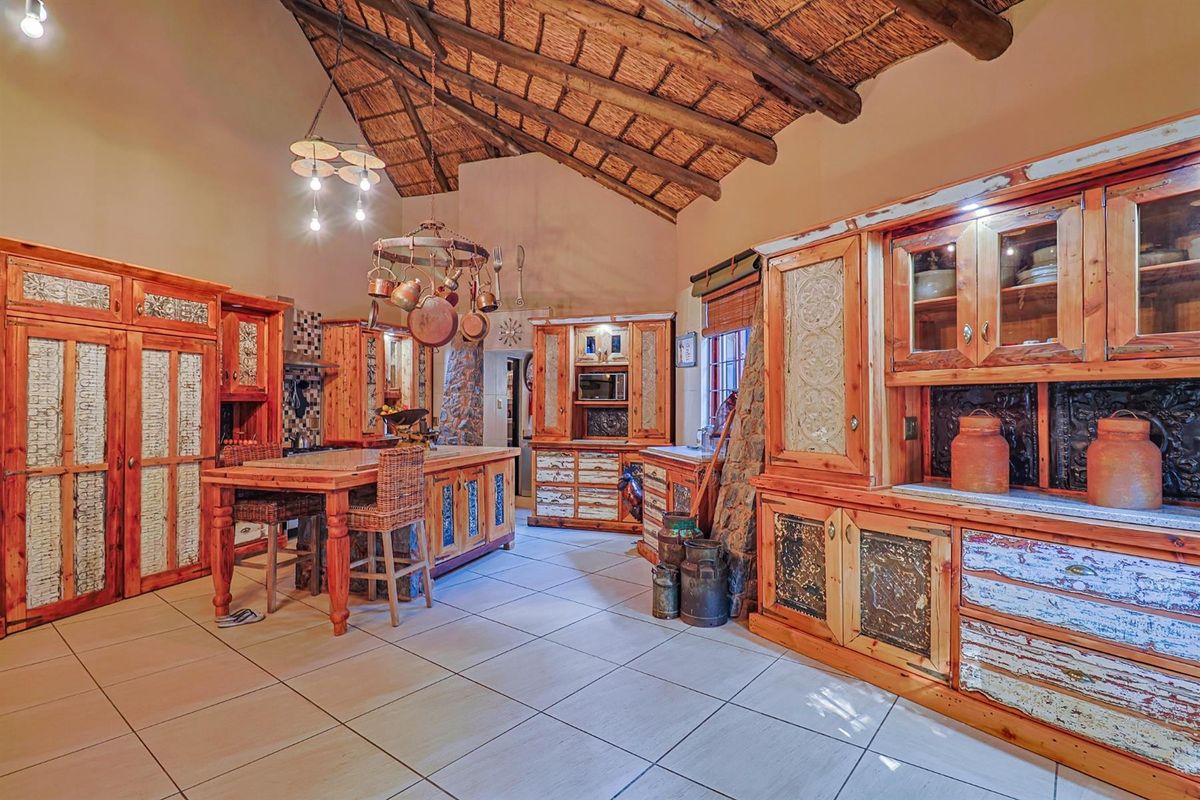 Spacious rustic kitchen featuring exposed thatch ceilings, timber roof trusses, custom wooden cabinetry, a central island, and stone architectural detailing.
