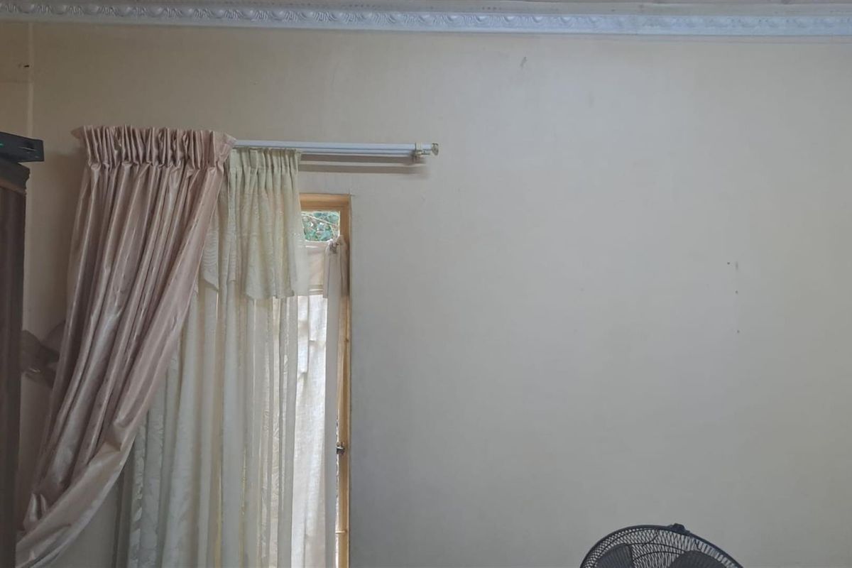 A bedroom interior featuring decorative ceiling cornicing and a window with curtain fixtures.