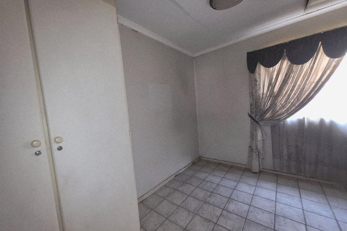 A compact bedroom featuring built-in cupboards, tiled flooring, and a window with existing curtain fixtures.