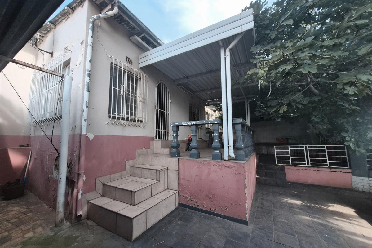 Rear exterior view of the townhouse featuring a covered patio area, tiled steps, and security bars on windows and doors.