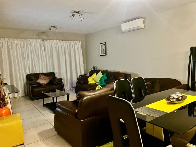 Open-plan living and dining area featuring tiled flooring, track lighting, and a wall-mounted split-system air conditioner.