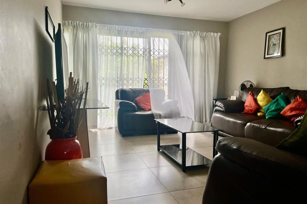 A living room featuring tiled flooring and a sliding glass door with a security gate, providing access to the exterior.