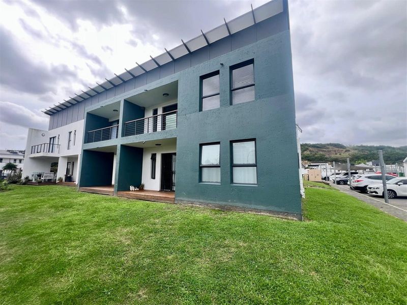 Rear view of a modern apartment building featuring covered ground floor patios, upper-level balconies with metal railings, and timber decking.