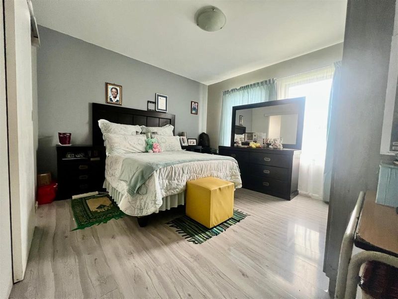 A well-lit bedroom featuring light-toned laminate flooring and neutral grey walls, providing a comfortable and functional living space.