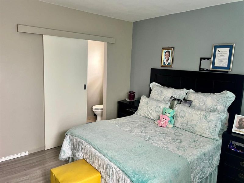 A bedroom featuring laminate flooring and a sliding door providing access to an en-suite toilet.