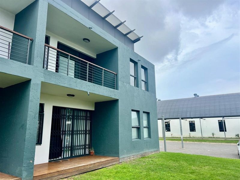Exterior view of a modern apartment building featuring a ground floor timber deck, private balcony with metal railings, and secure sliding glass doors.