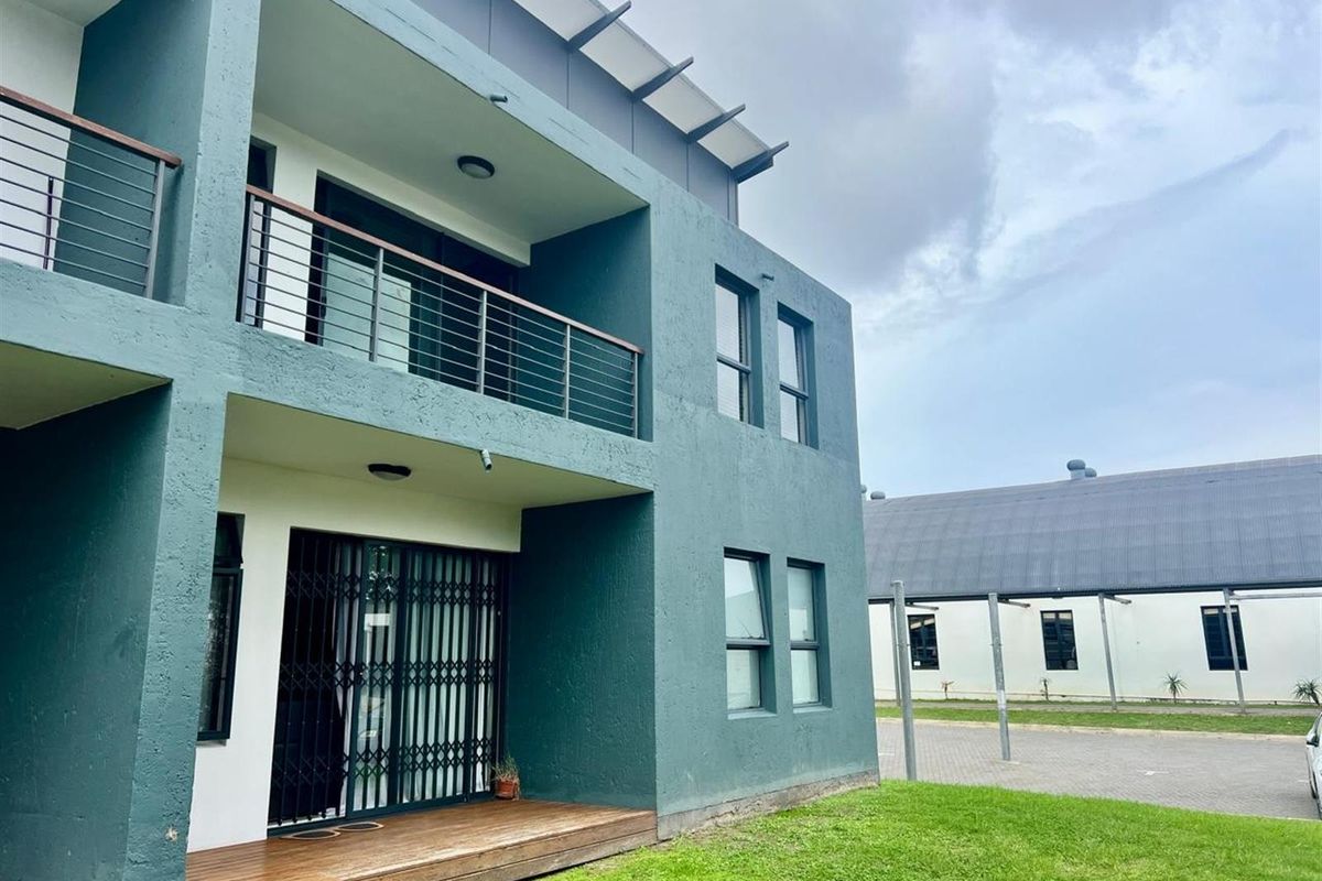 Exterior view of a modern apartment building featuring a ground floor timber deck, private balcony with metal railings, and secure sliding glass doors.