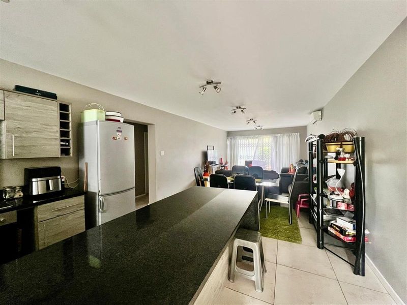 Open-plan living area featuring a modern kitchen with granite island, tiled flooring, and integrated air conditioning, flowing into a combined dining and lounge space.