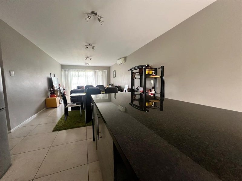 Open-plan living area featuring a sleek granite kitchen island, tiled flooring, and modern track lighting, creating a functional and connected space.