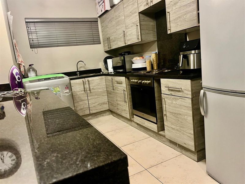 A functional kitchen featuring wood-look cabinetry, dark granite countertops, a built-in oven and hob, and tiled flooring.