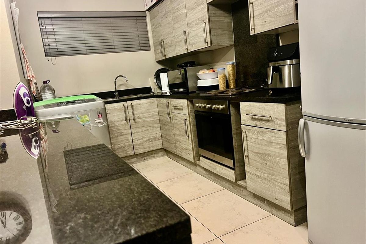 A functional kitchen featuring wood-look cabinetry, dark granite countertops, a built-in oven and hob, and tiled flooring.