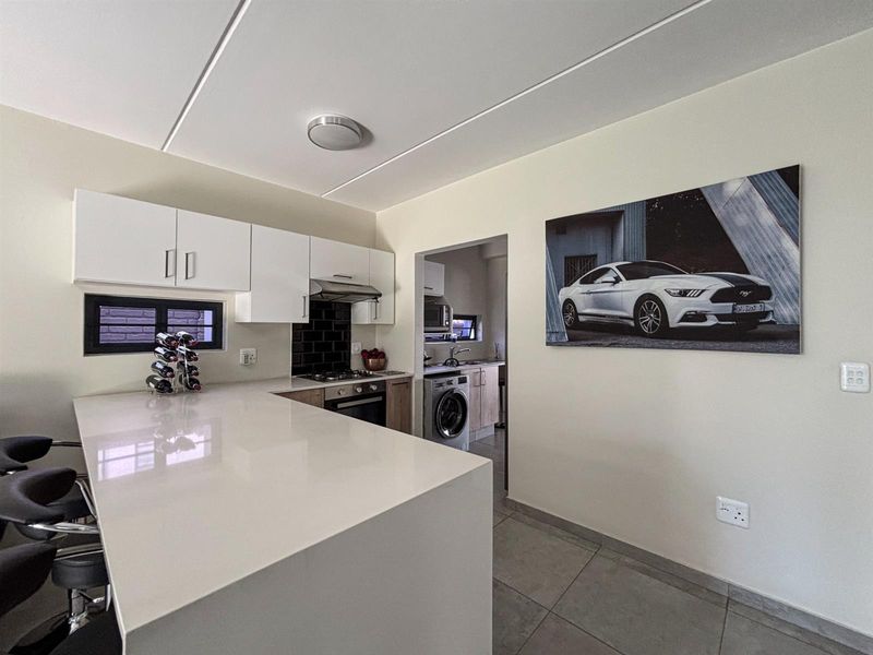 Modern open-plan kitchen featuring a large quartz breakfast bar, built-in oven, gas hob, and sleek white cabinetry, seamlessly connected to a functional scullery area.