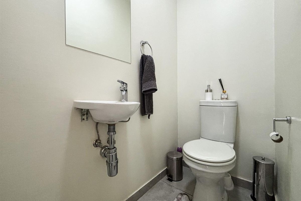 A compact guest bathroom featuring a wall-mounted basin, modern chrome fixtures, and a standard toilet with neutral wall finishes.