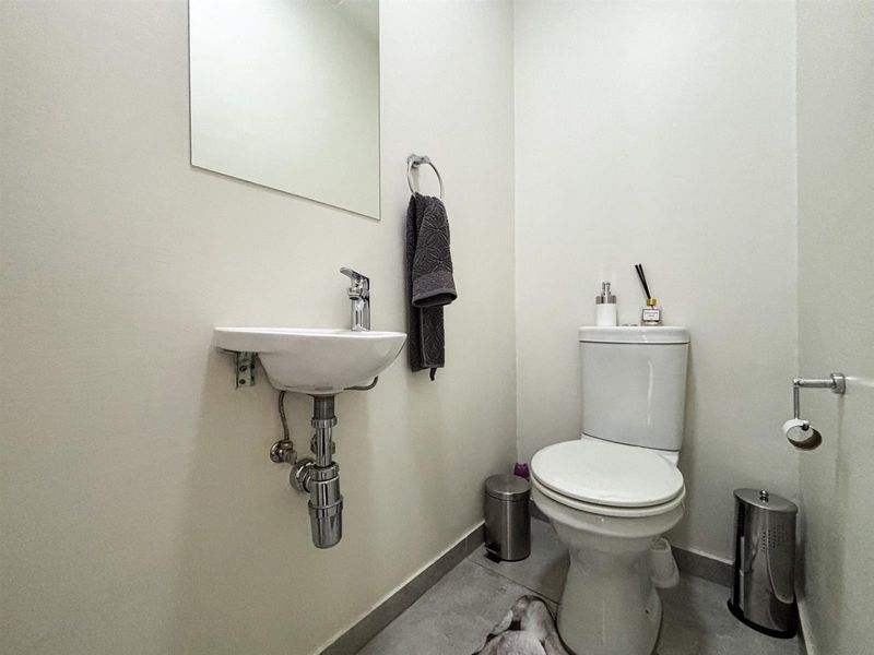 A compact guest bathroom featuring a wall-mounted basin, modern chrome fixtures, and a standard toilet with neutral wall finishes.