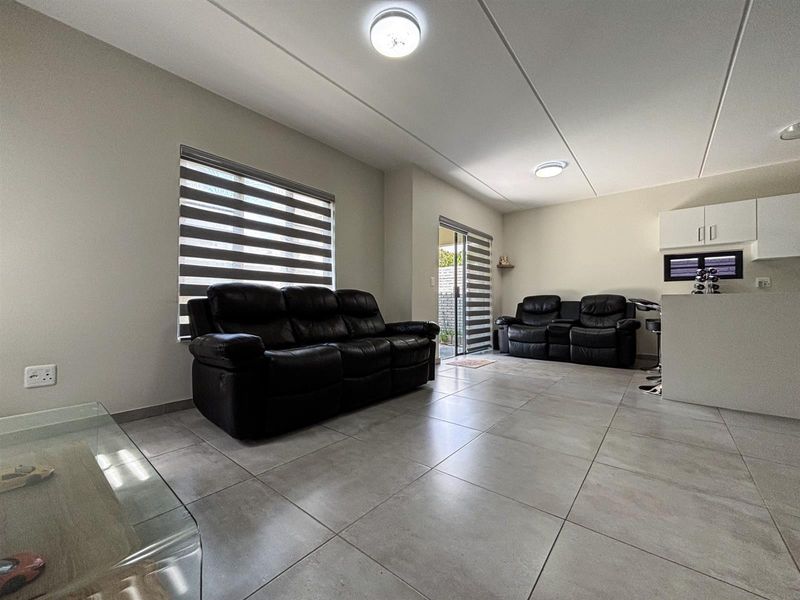 A bright open-plan living and kitchen area featuring large format floor tiles, modern zebra blinds, and a functional kitchen island with built-in cabinetry.
