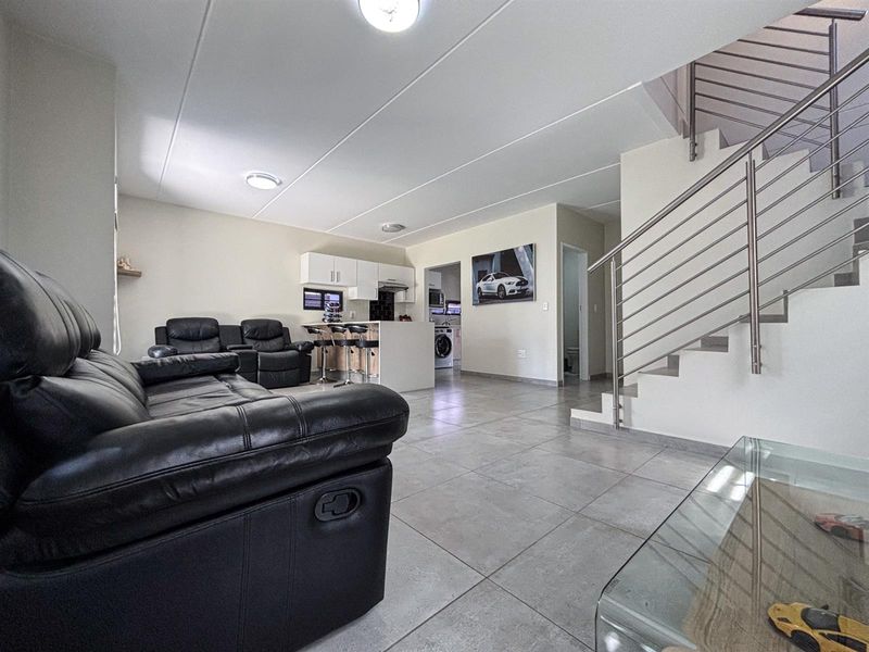 Open plan living area featuring tiled floors, a modern staircase with stainless steel railings, and a compact kitchen with built-in cabinetry.