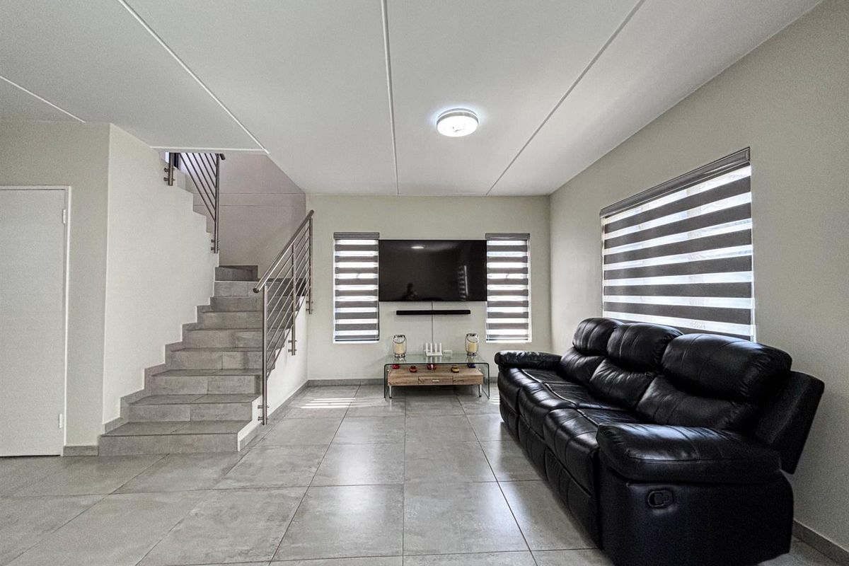 Modern living room featuring large format floor tiles, a sleek staircase with stainless steel balustrades, and contemporary roller blinds.