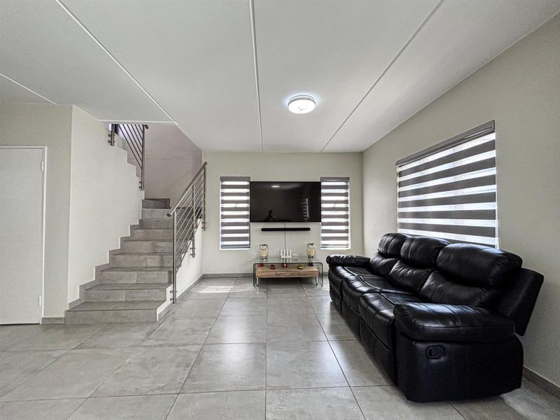 Modern living room featuring large format floor tiles, a sleek staircase with stainless steel balustrades, and contemporary roller blinds.