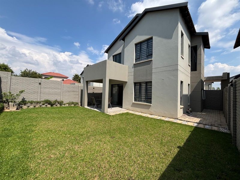 Rear view of a two-story house featuring a covered patio, paved walkway, and a well-maintained private garden with boundary walling.