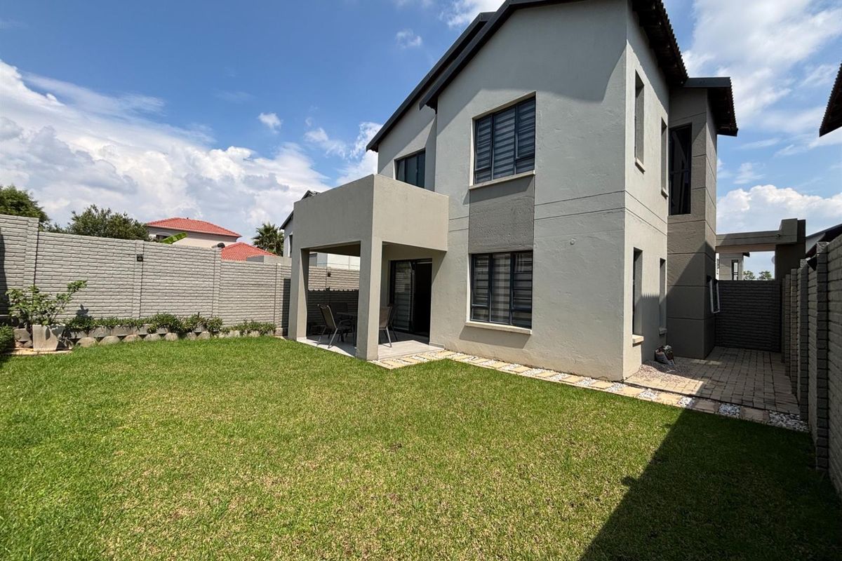 Rear view of a two-story house featuring a covered patio, paved walkway, and a well-maintained private garden with boundary walling.