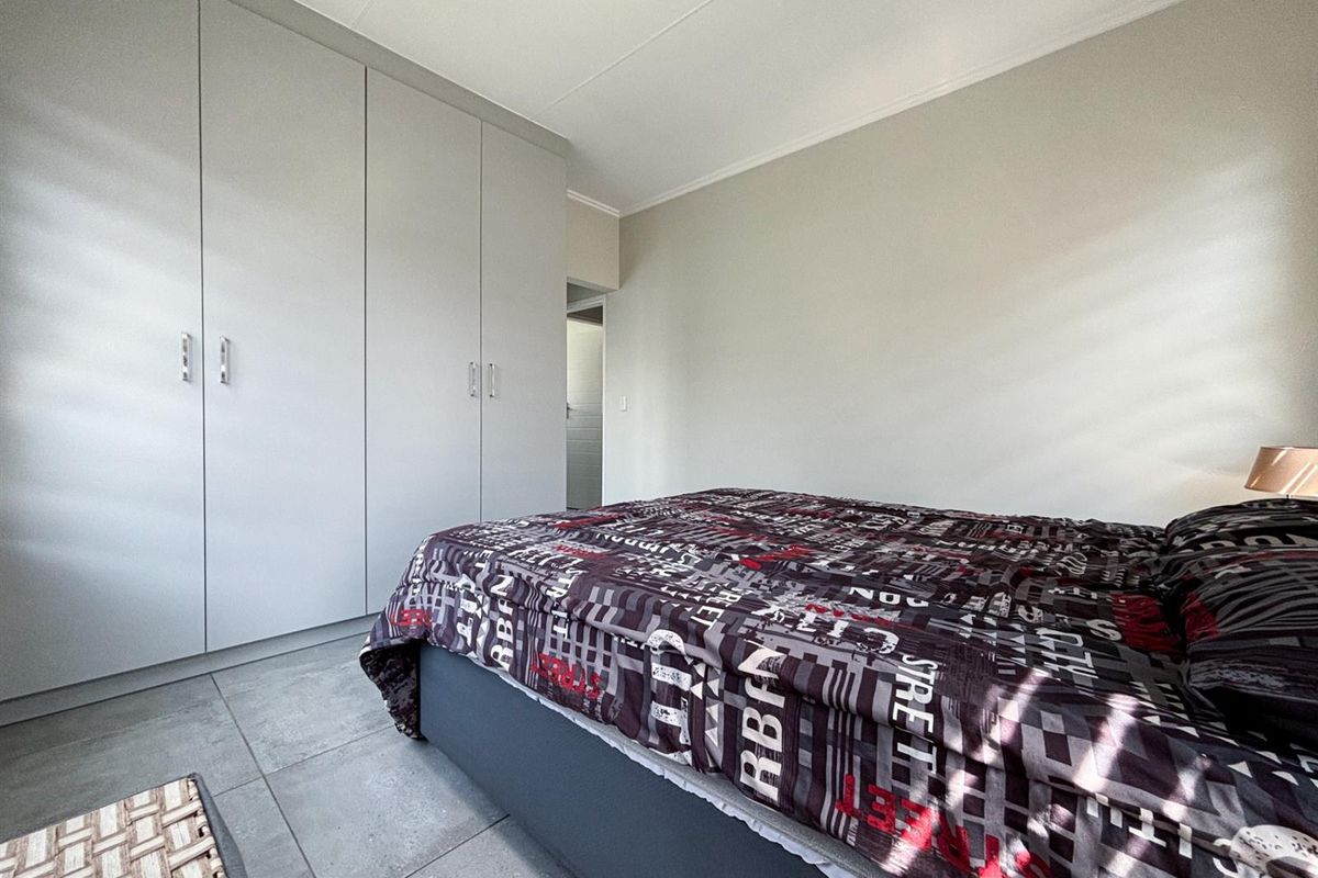A clean bedroom featuring neutral walls, modern grey floor tiles, and ample built-in cupboard storage.