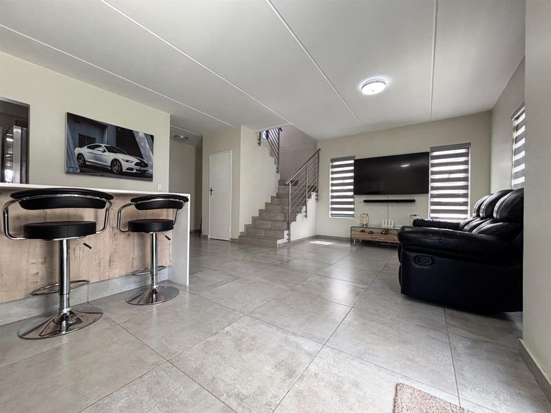 Spacious open-plan living area featuring large format floor tiles, a modern staircase with metal balustrades, and a breakfast counter.