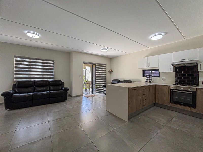 Modern open-plan living area featuring a contemporary kitchen with stone countertops, built-in appliances, and seamless access to an outdoor patio through sliding glass doors.