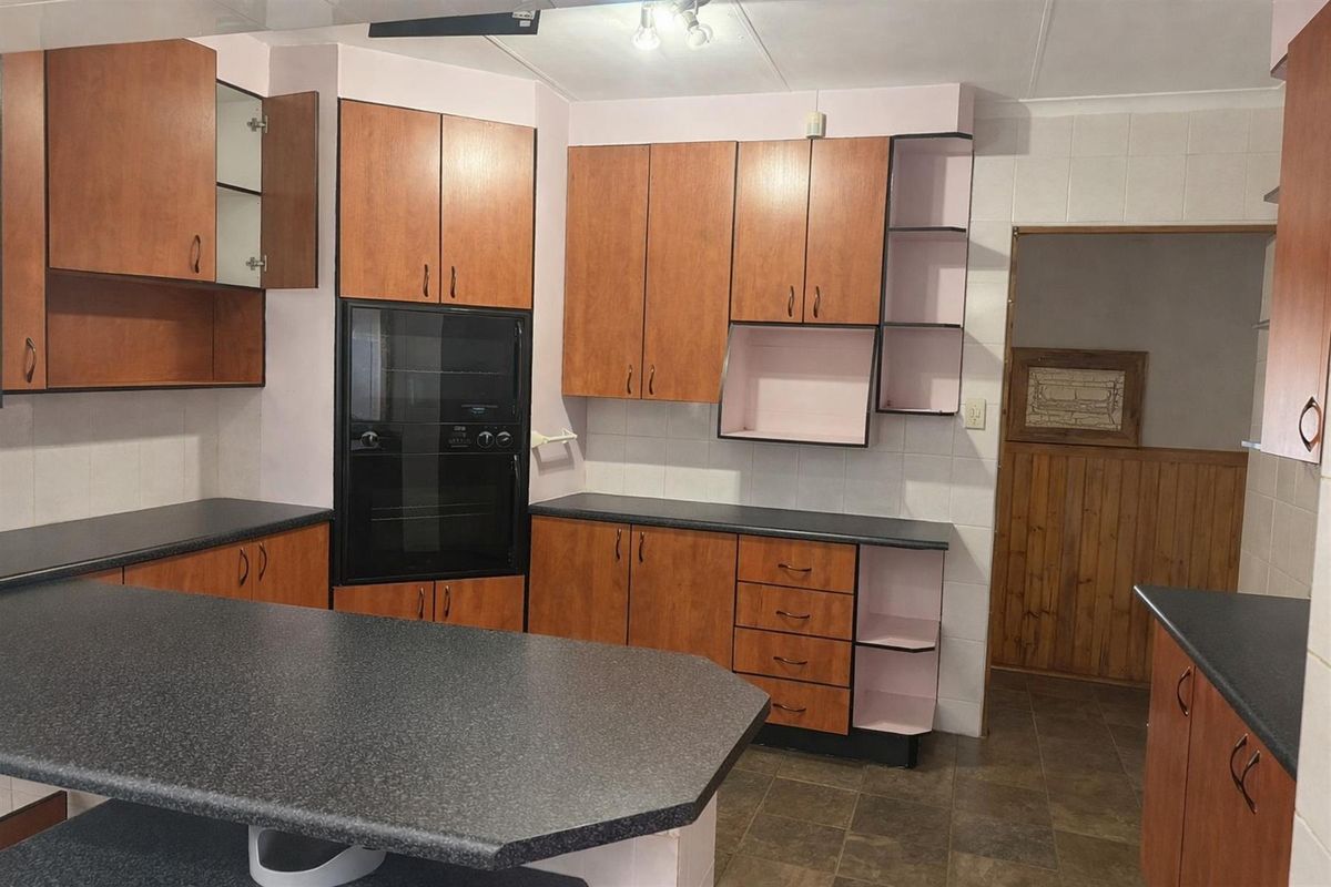 A functional kitchen featuring built-in oven, ample laminate cabinetry, dark countertops, and tiled flooring, offering a dated but well-maintained layout.
