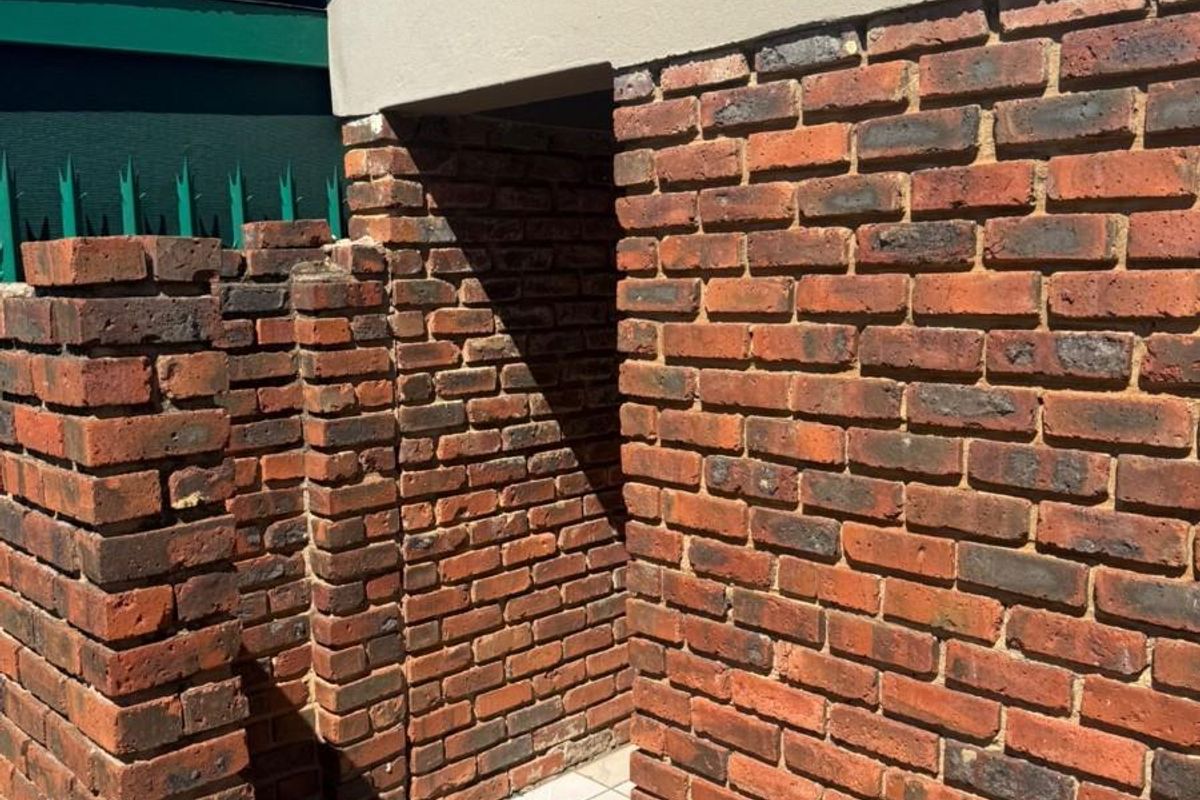 A view of a brick-walled exterior passage or utility area featuring tiled flooring and exposed face brick construction.