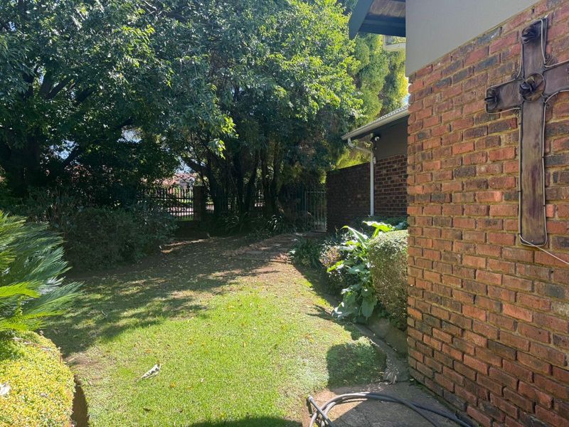 A private garden area featuring a brick exterior wall, mature trees, and a metal gate entrance.