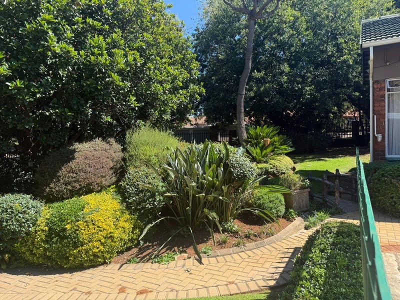 A well-maintained garden area featuring a paved walkway, mature landscaping, and established trees, providing a pleasant outdoor space.