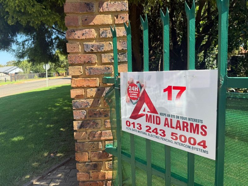 A view of the property entrance featuring a brick pillar and metal security fencing with an attached security company signage.