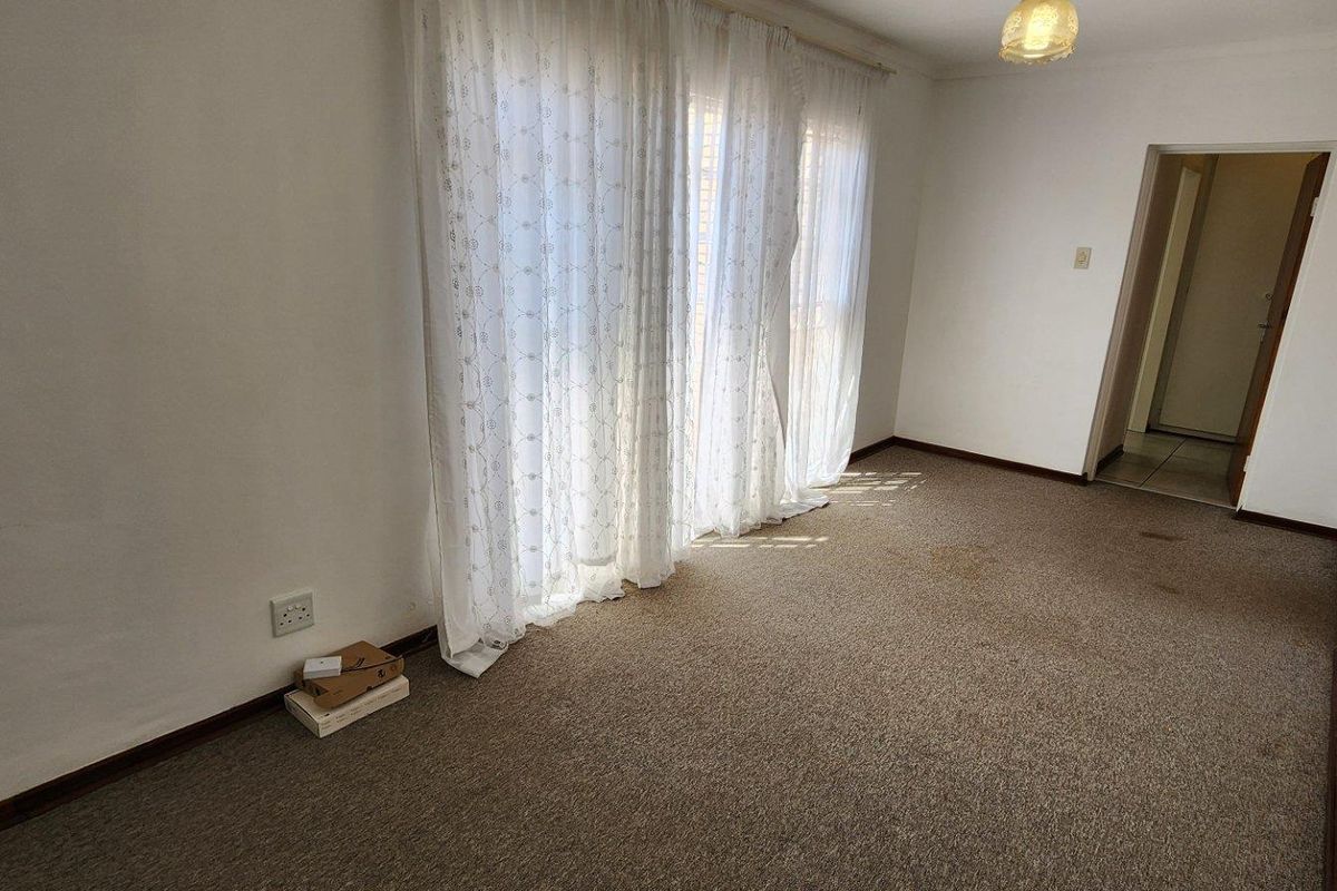 An empty living room featuring neutral walls, carpeted flooring, and large windows with curtains, providing a blank canvas for potential interior updates.