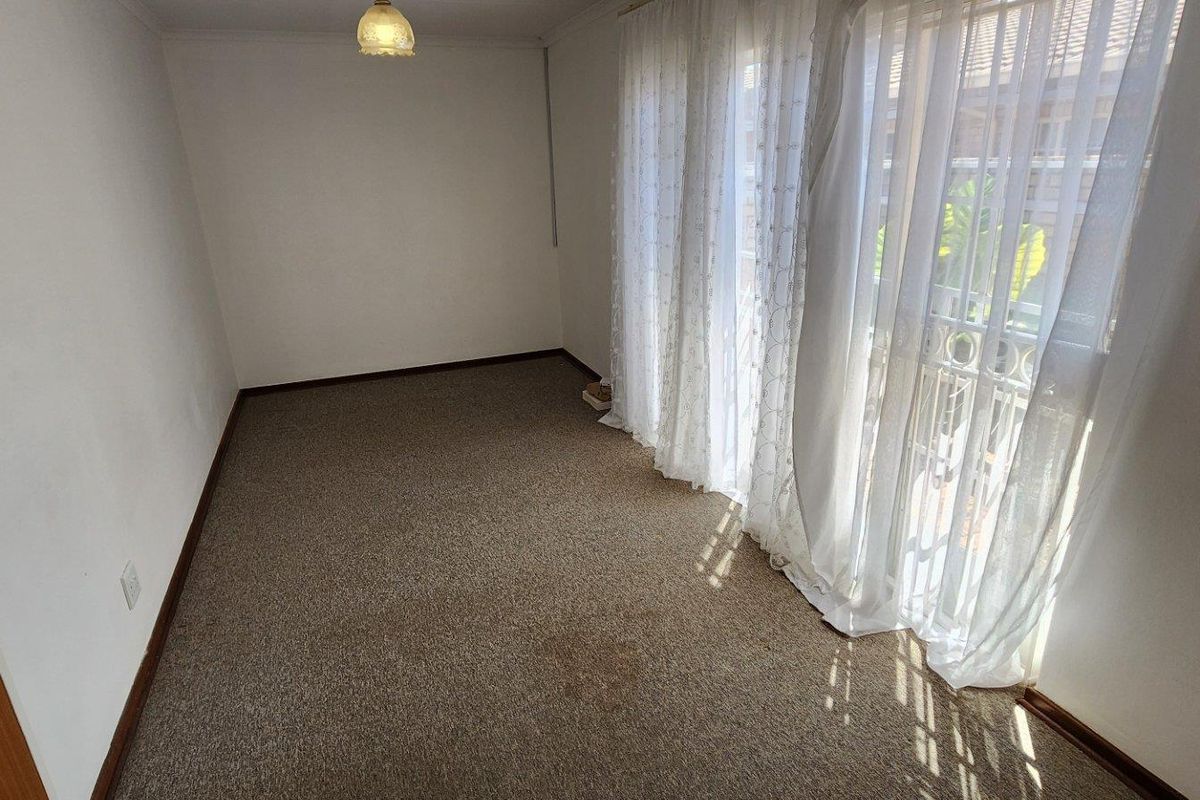 A vacant bedroom featuring neutral walls, carpeted flooring, and large windows with sheer curtains allowing natural light.