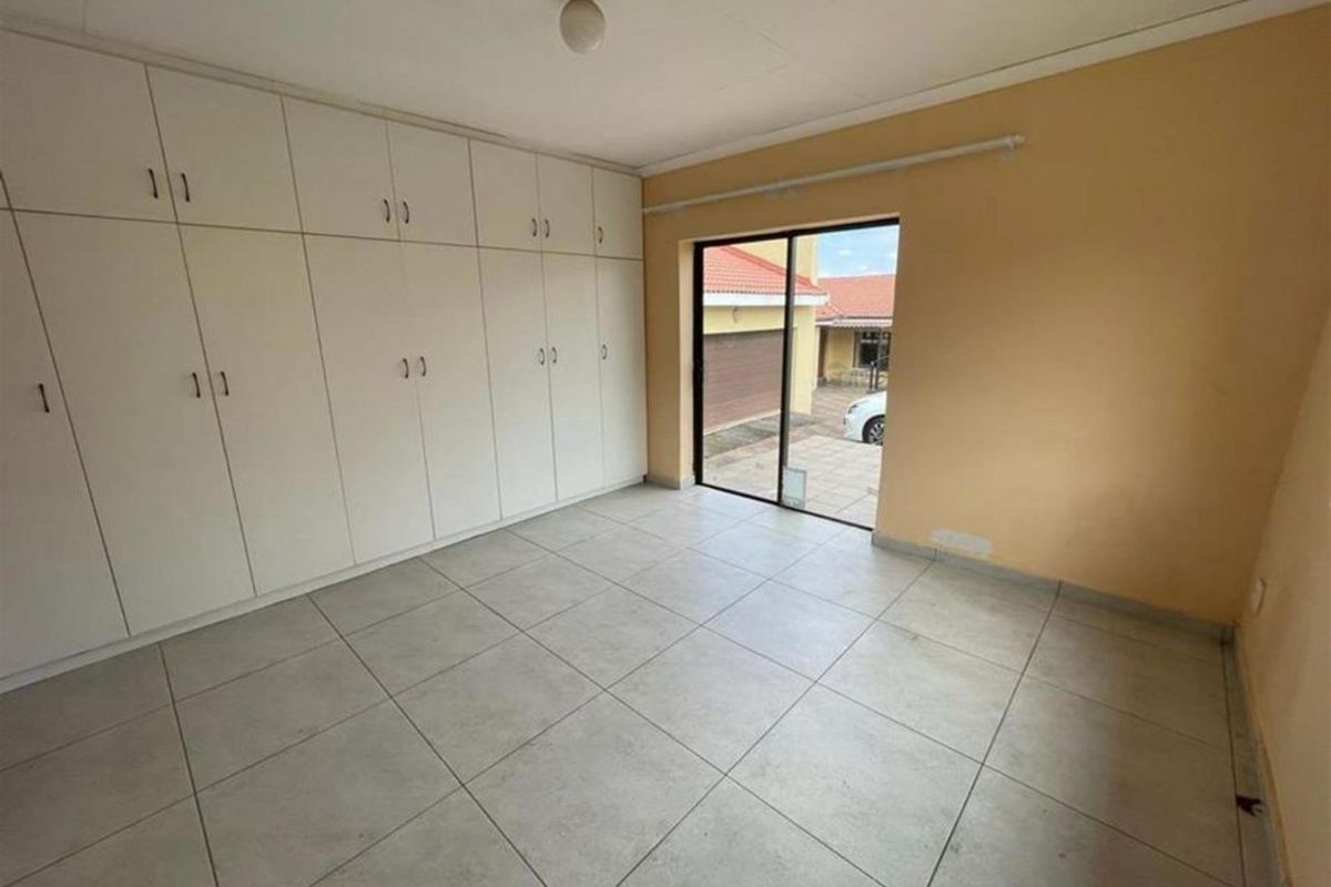 An empty bedroom featuring extensive built-in storage cupboards, tiled flooring, and a sliding glass door providing access to the exterior.