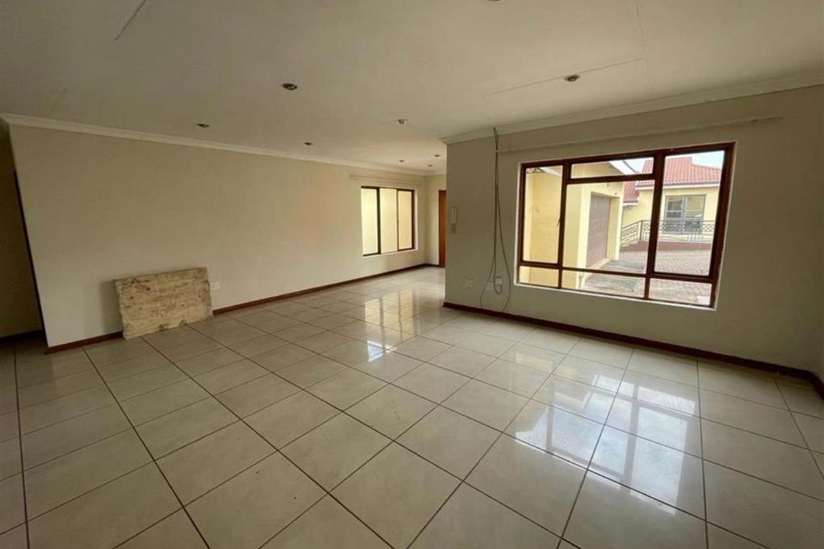 A spacious, empty living area featuring neutral tiled flooring, recessed lighting, and large windows providing natural light and views of the exterior.