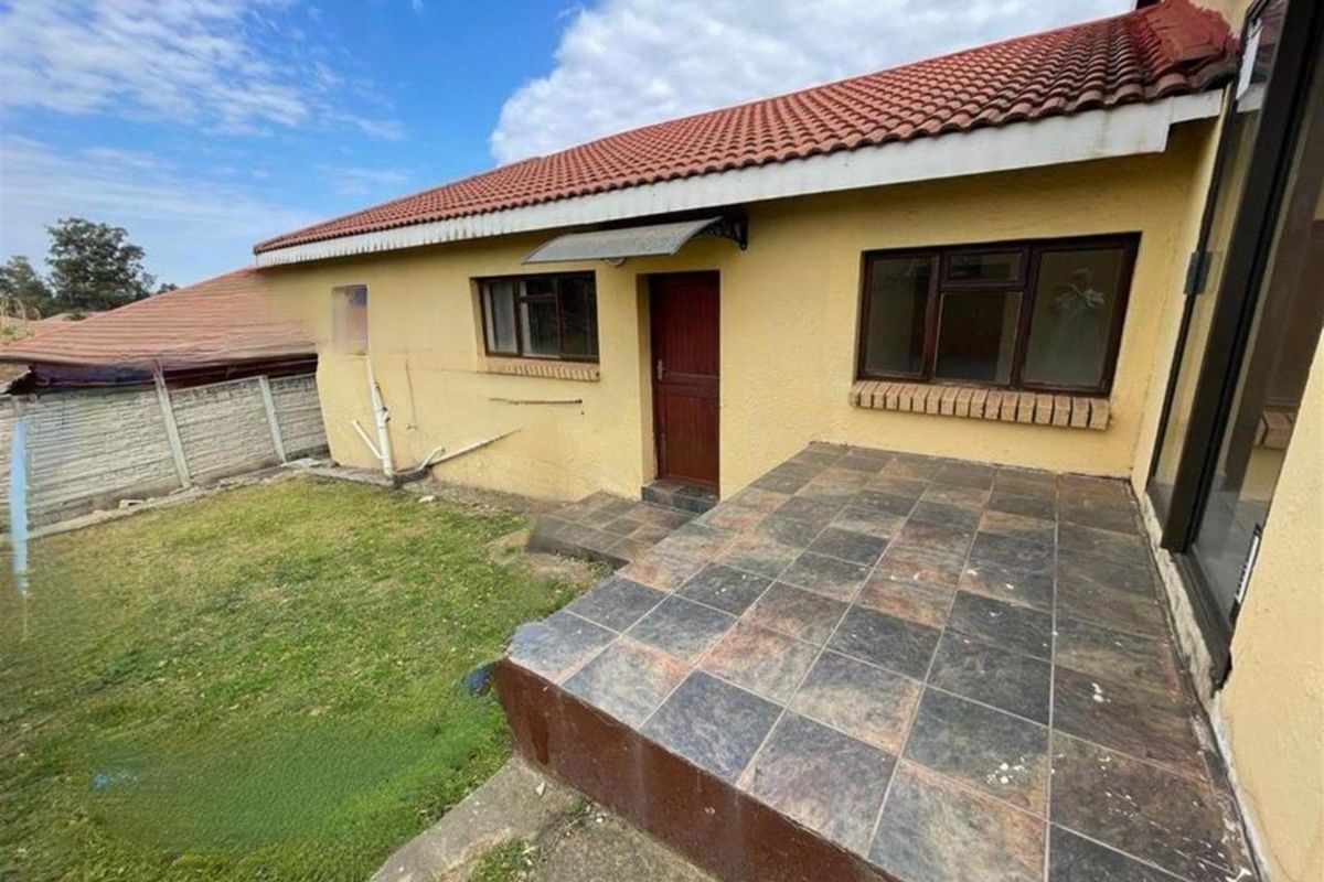 Rear exterior view of the townhouse featuring a tiled patio area, small garden space, and terracotta roof tiles.
