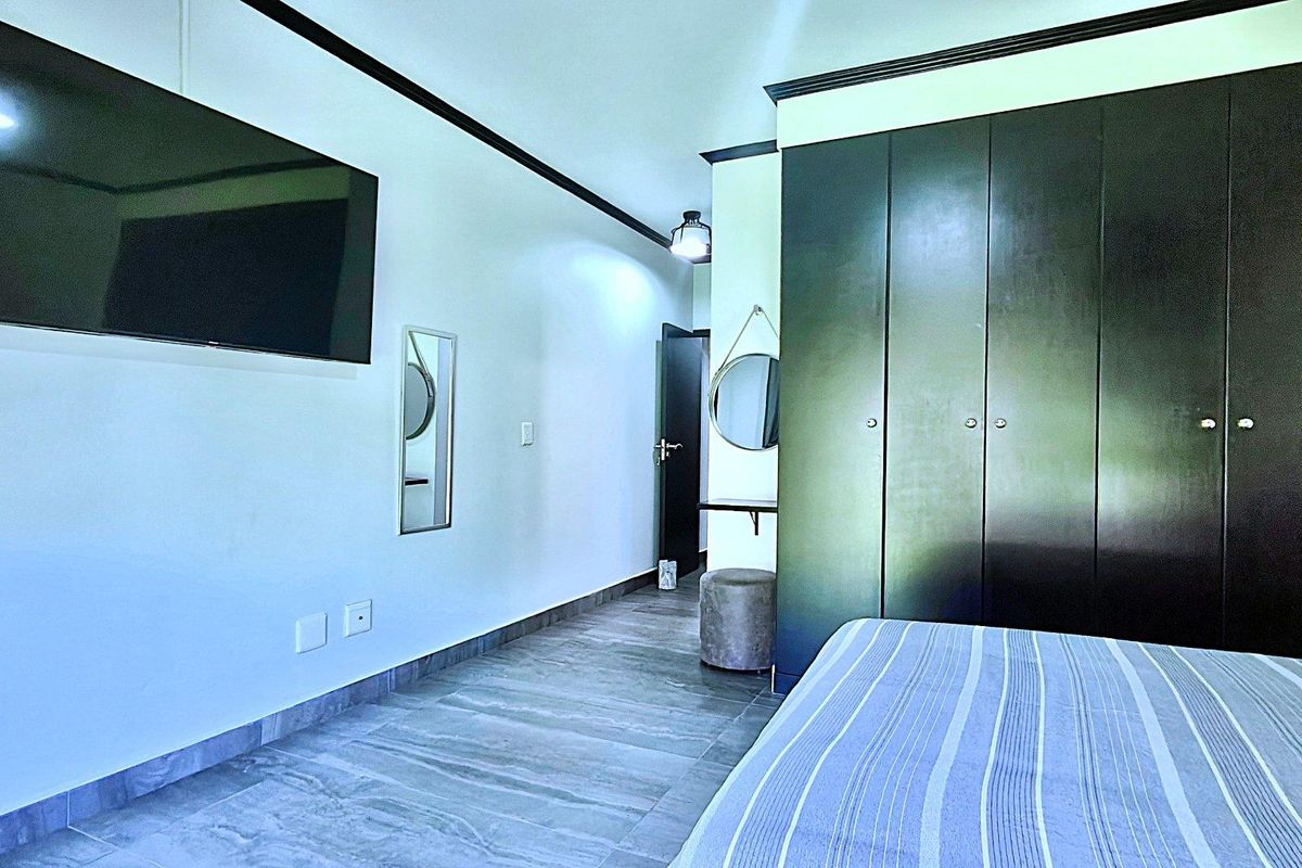 A well-maintained bedroom featuring built-in dark wood cabinetry, tiled flooring, and modern crown molding.