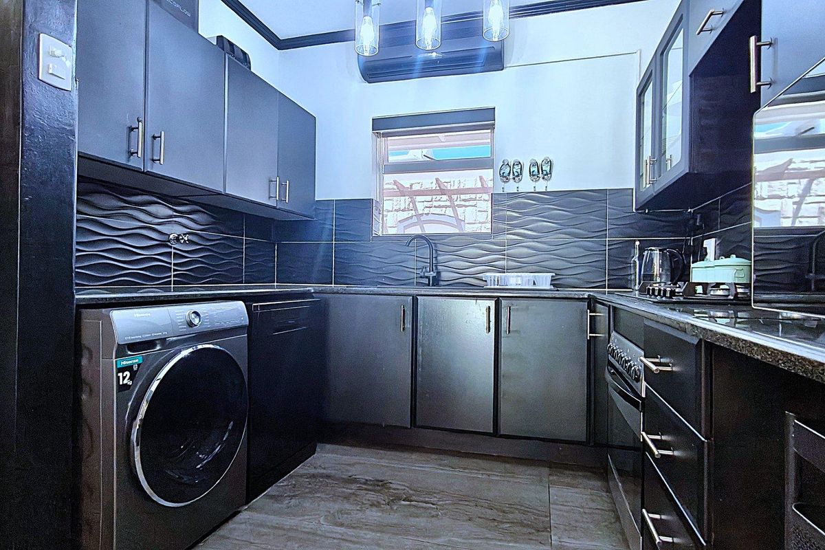 Modern kitchen featuring dark cabinetry, textured backsplash tiling, integrated oven and hob, and dedicated space for laundry appliances.
